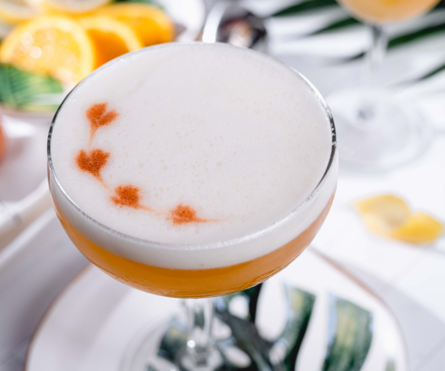 Close up image of a whiskey sour with egg white foam and a heart design made with bitters